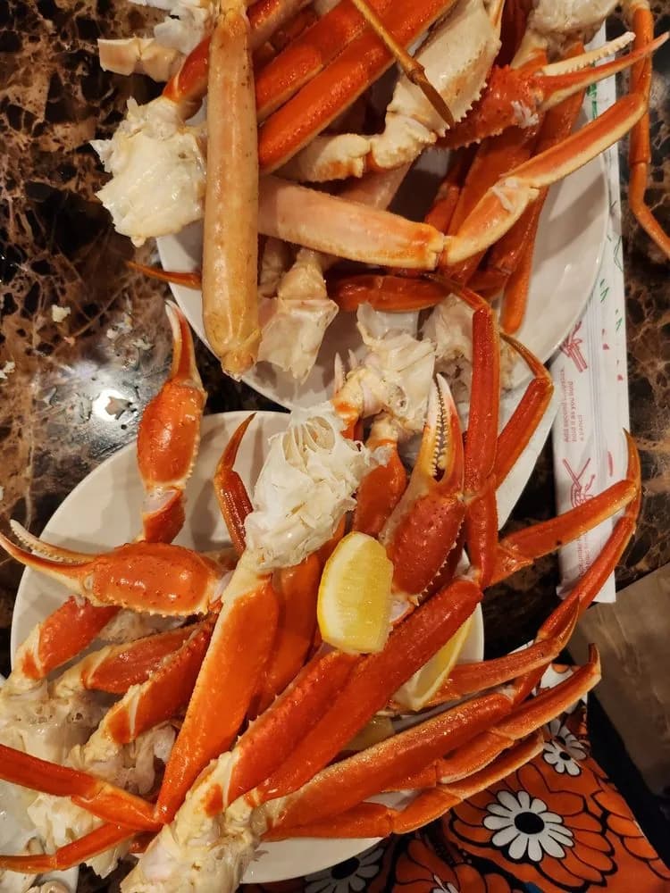 Two plates stacked with snow crab legs and a lemon wedge on a marble table