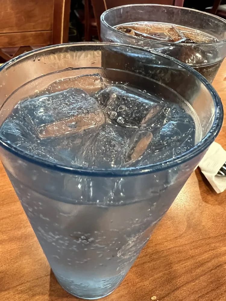 Two tall glasses of iced water on a wooden dining table