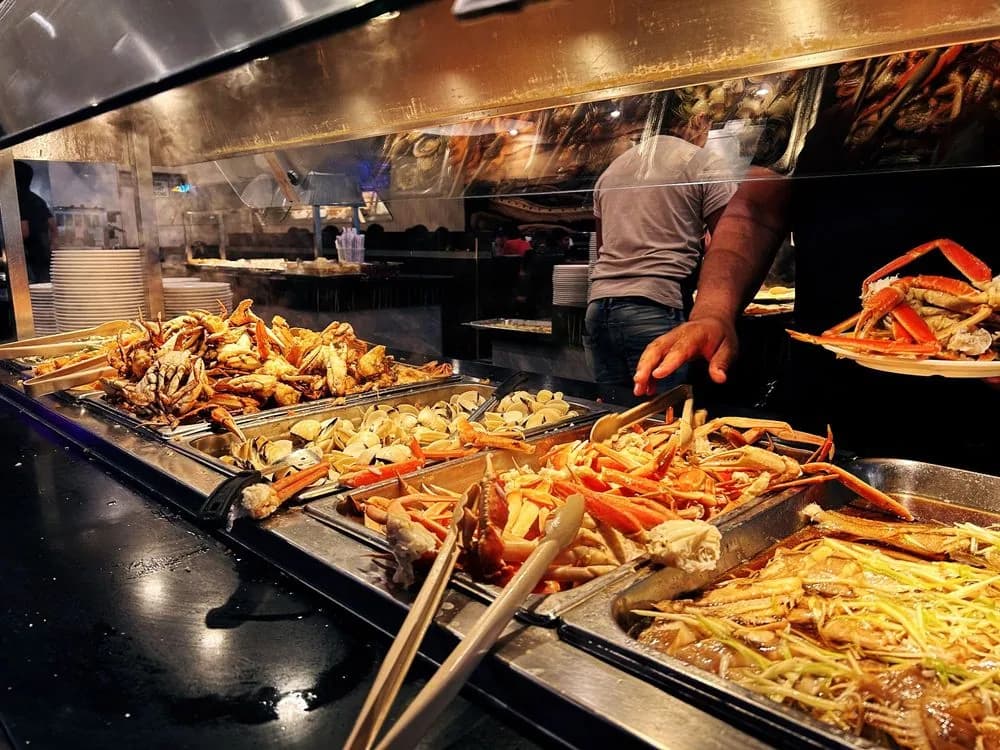 Trays of crab legs, whole crab and clams on the hot seafood bar as a diner fills a plate