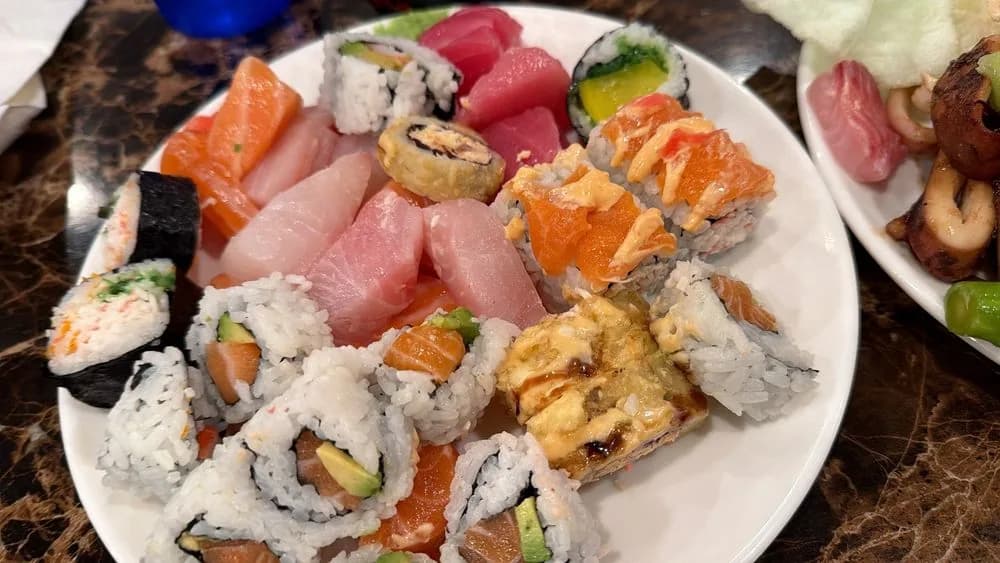 A plate of assorted sushi rolls and sashimi slices carried back to a table