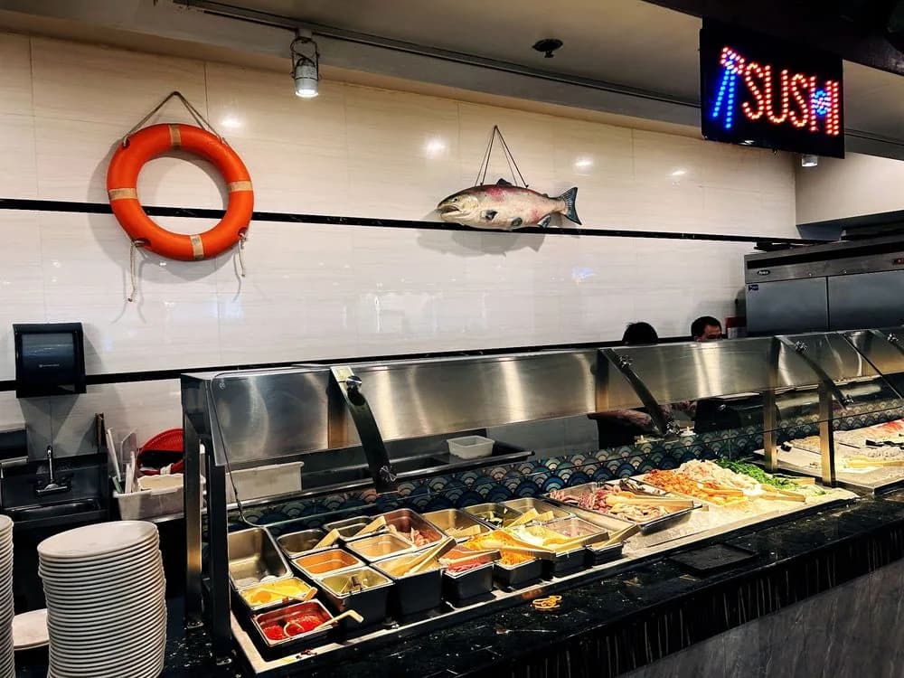 The sushi counter with a neon sushi sign, stacked plates and chilled trays
